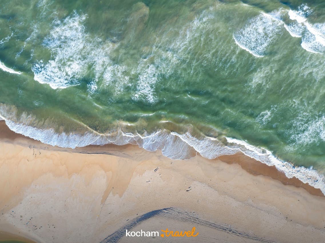 Widok z lotu ptaka na piaszczystą plażę i fale oceanu.