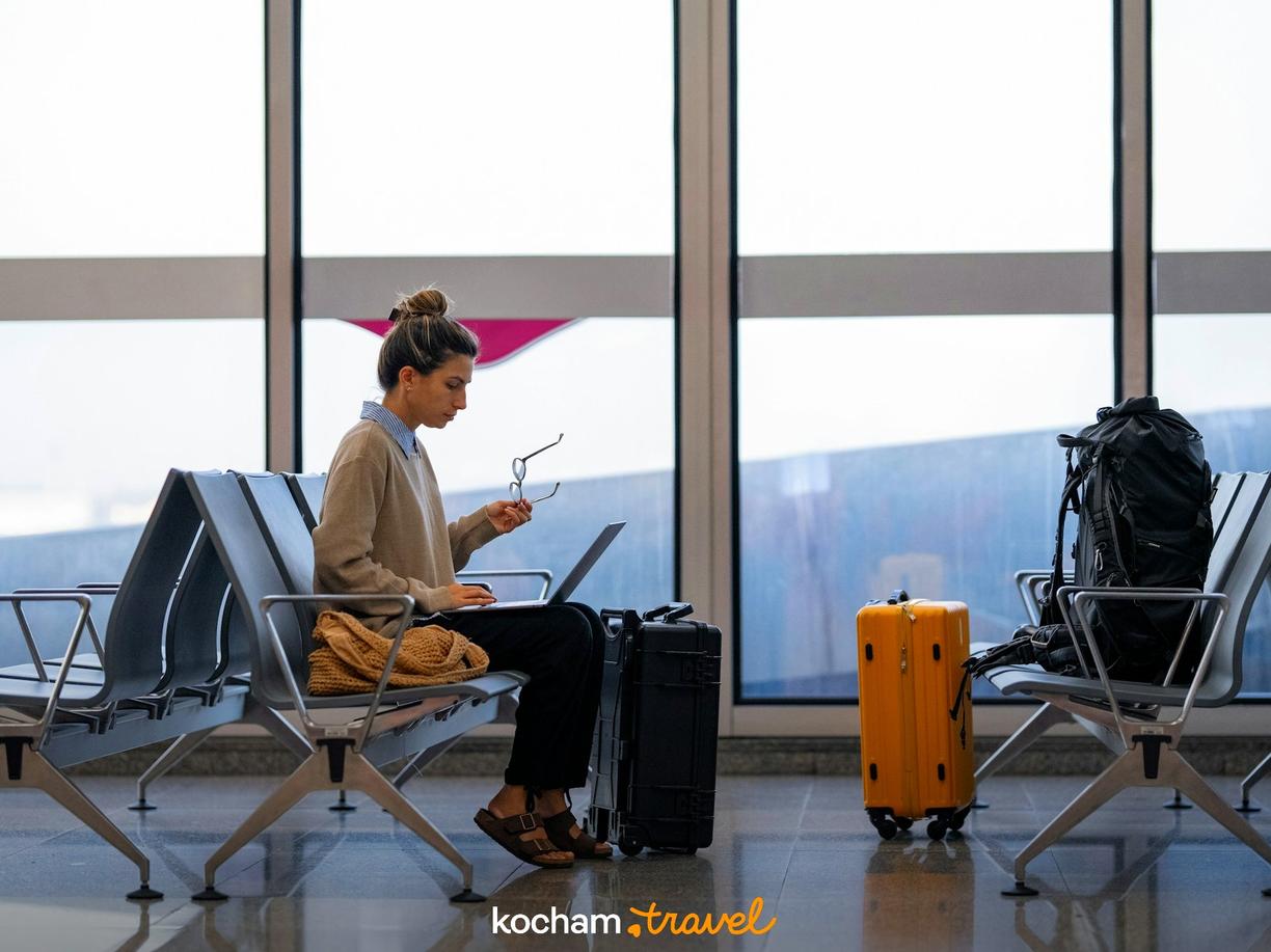 Podróżna pracuje na laptopie, siedząc na ławce w terminalu lotniczym.