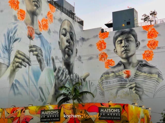 Mural przedstawiający trzech chłopców z pomarańczowymi różami na ścianie budynku.