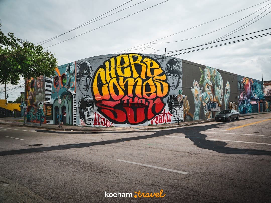 Kolorowy mural street art na rogu budynku z napisem "Here Comes The Sun".