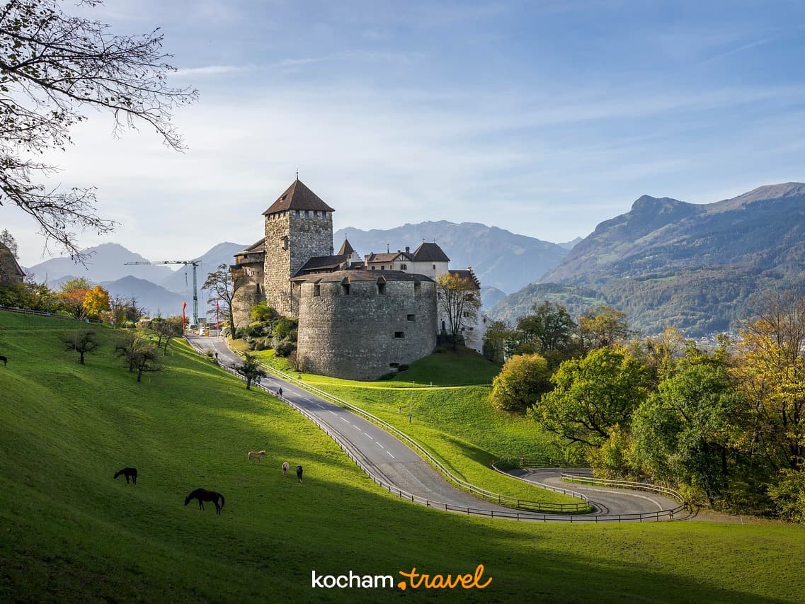 Zamek Vaduz, Liechtenstein, zielone wzgórza, góry, kręta droga, konie.