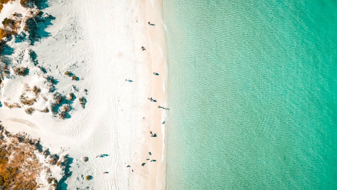 Biała piaszczysta plaża, turkusowa woda, ludzie, widok z lotu ptaka.