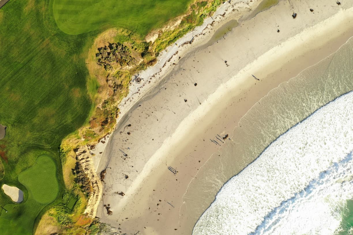 Pole golfowe, piaszczysta plaża, oceaniczne fale i spacerujący ludzie.