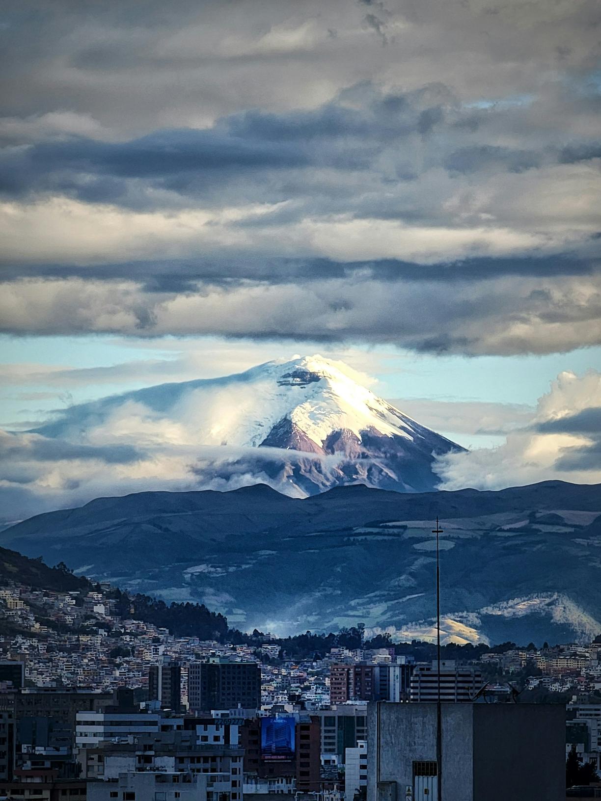 Majestatyczny wulkan Cotopaxi górujący nad Quito, częściowo w chmurach.