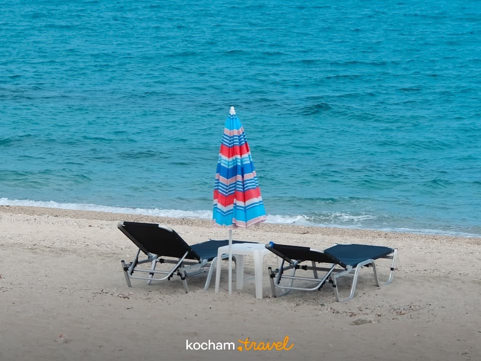 Piaszczysta plaża, turkusowa woda, parasol i leżaki, wakacyjny relaks.