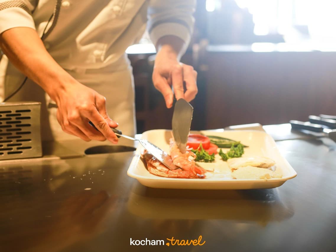 Szef kuchni serwujący krewetki i warzywa na talerzu w restauracji.