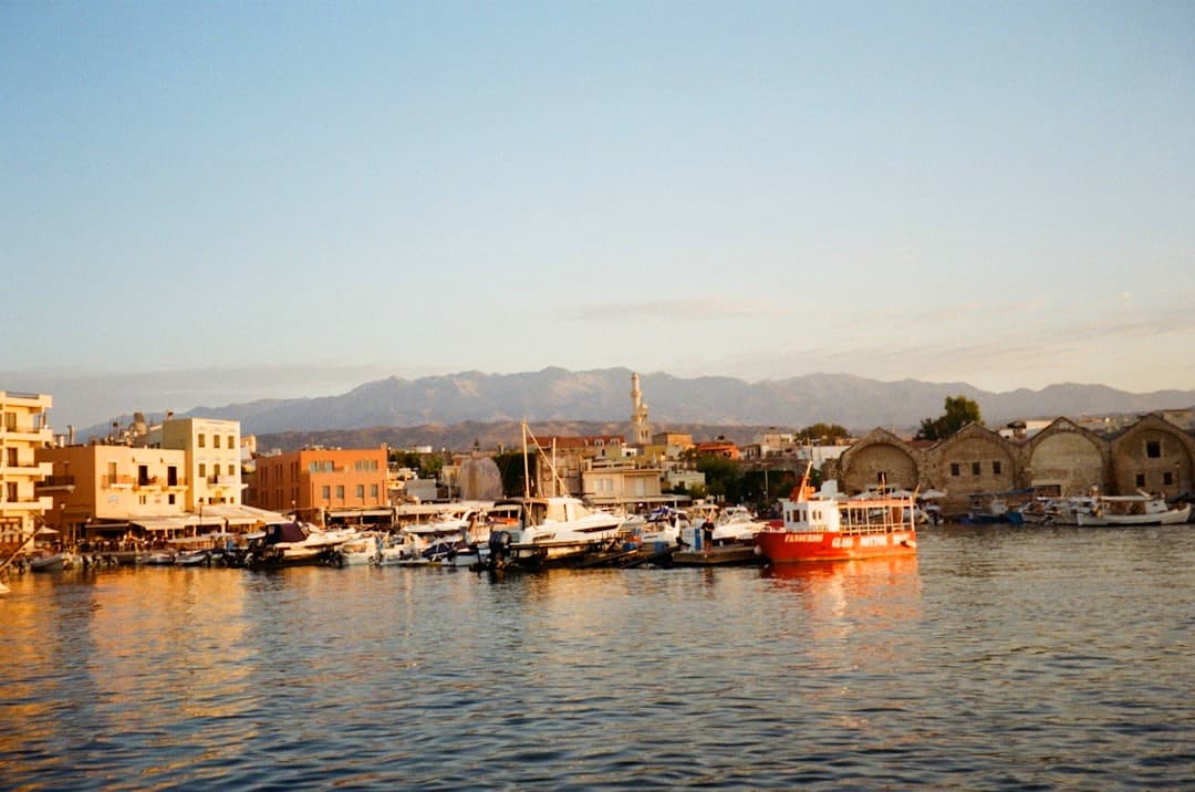 Chania, Kreta: malowniczy port, łodzie, zabytkowe budynki, góry, zachód słońca.